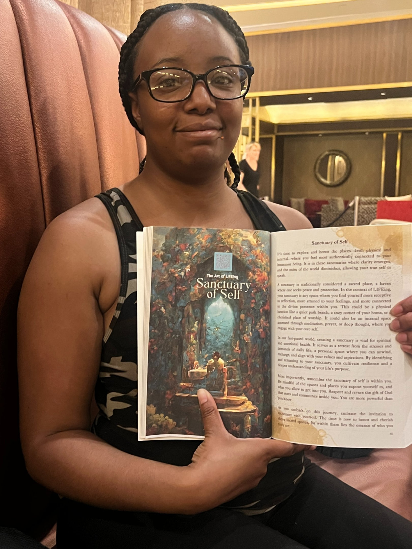 Reader seated holding The Art of LIFEing Journal open to the Sanctuary of Self chapter